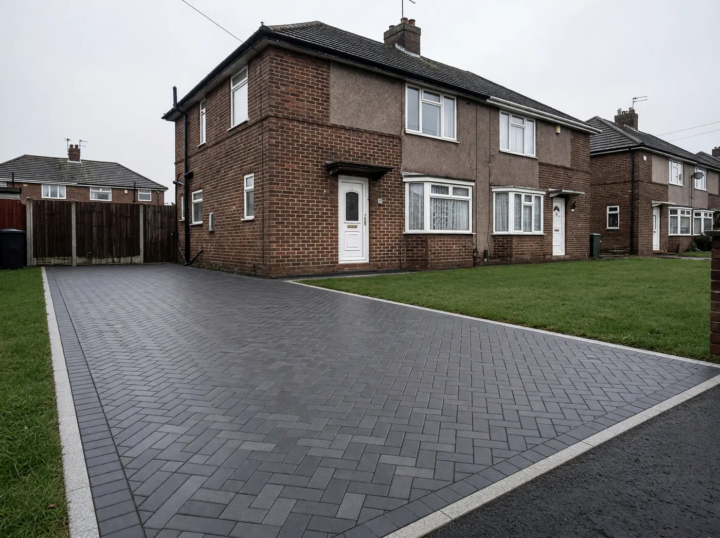 The same house and lawn with a new charcoal herringbone block driveway edged in pale granite