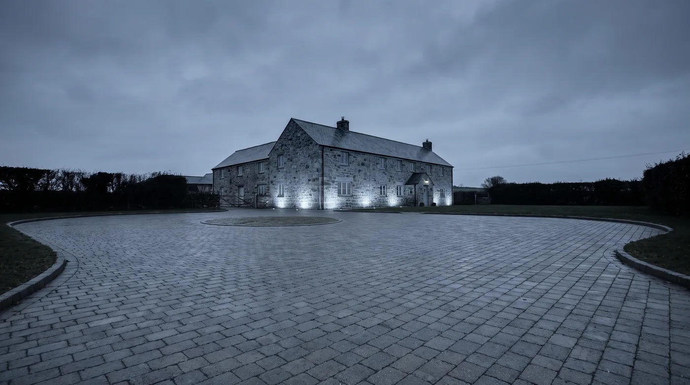 A finished charcoal block driveway at dusk with warm light from the house